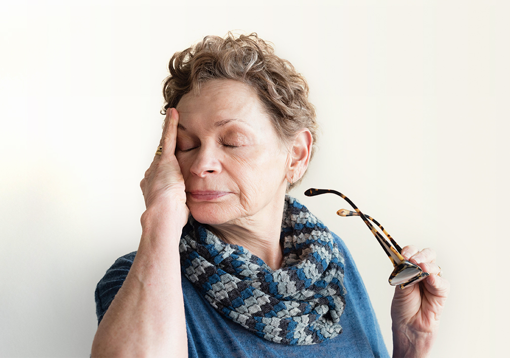A woman with dry eyes rubs her temples.